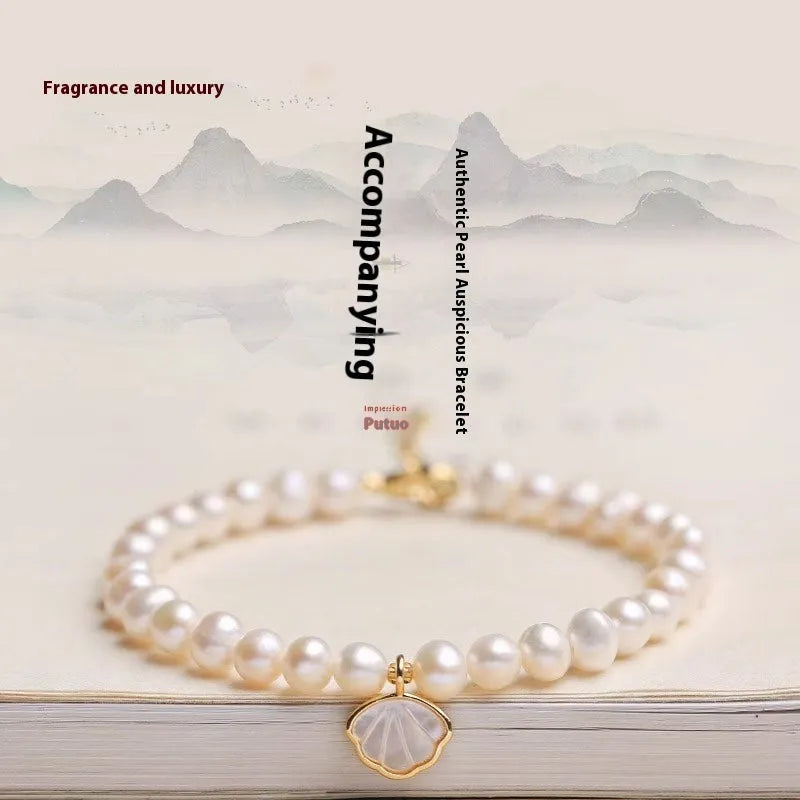 Women's freshwater pearl bracelet with fan-shaped charm on wrist, showing elastic and chain fastening options.