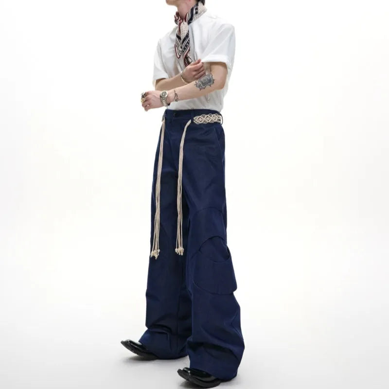 Man wearing dark blue straight-leg cotton jeans with loose fit, zipper decorations, and a tassel detail.