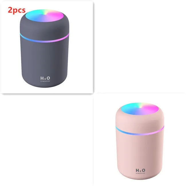 Pink USB desktop humidifier with LED lights and water tank on a wooden desk.