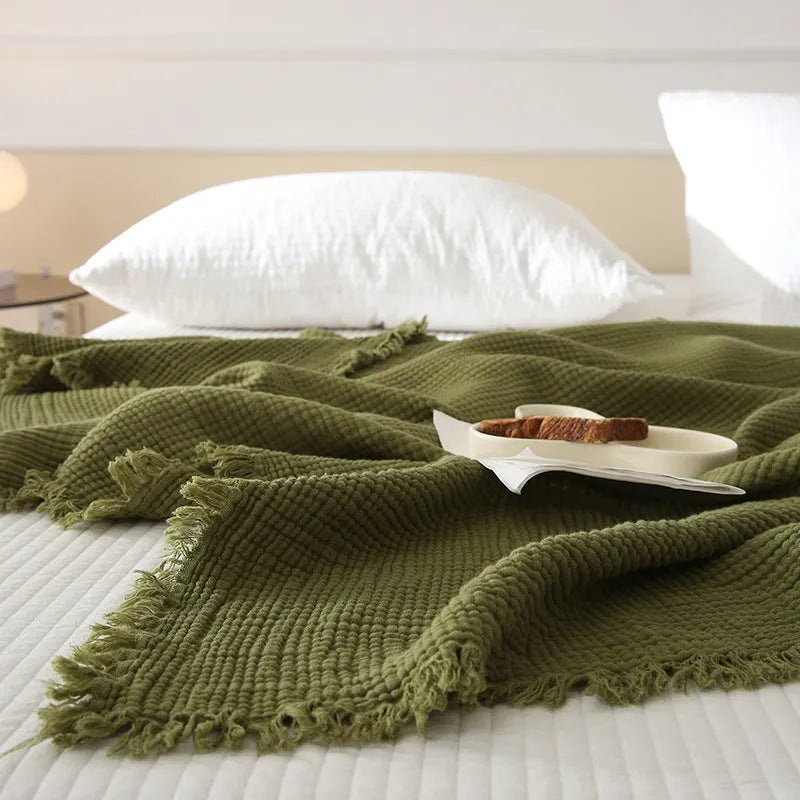 Cotton four-layer gauze blanket with tassel trim in various colours draped over a sofa.