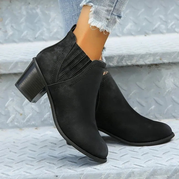Women's black ankle boots with pointed toe and thick square heel on wooden floor