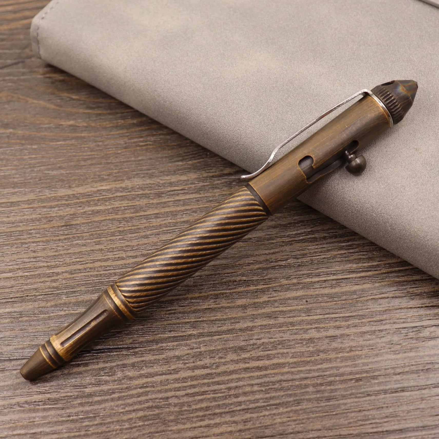 Close-up of a solid brass bolt action tactical pen with a press mechanism on a dark surface.