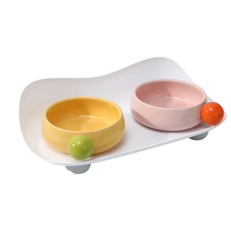 Raised ceramic double pet feeding bowl in pink, yellow, and pink yellow on a non-slip stand.