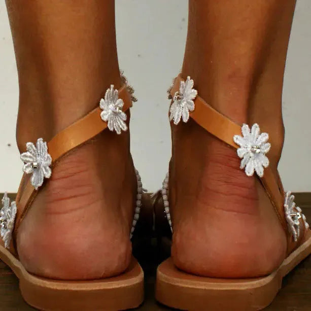 Brown women's Roman-style sandals with flat rubber sole and white floral decoration on the upper.