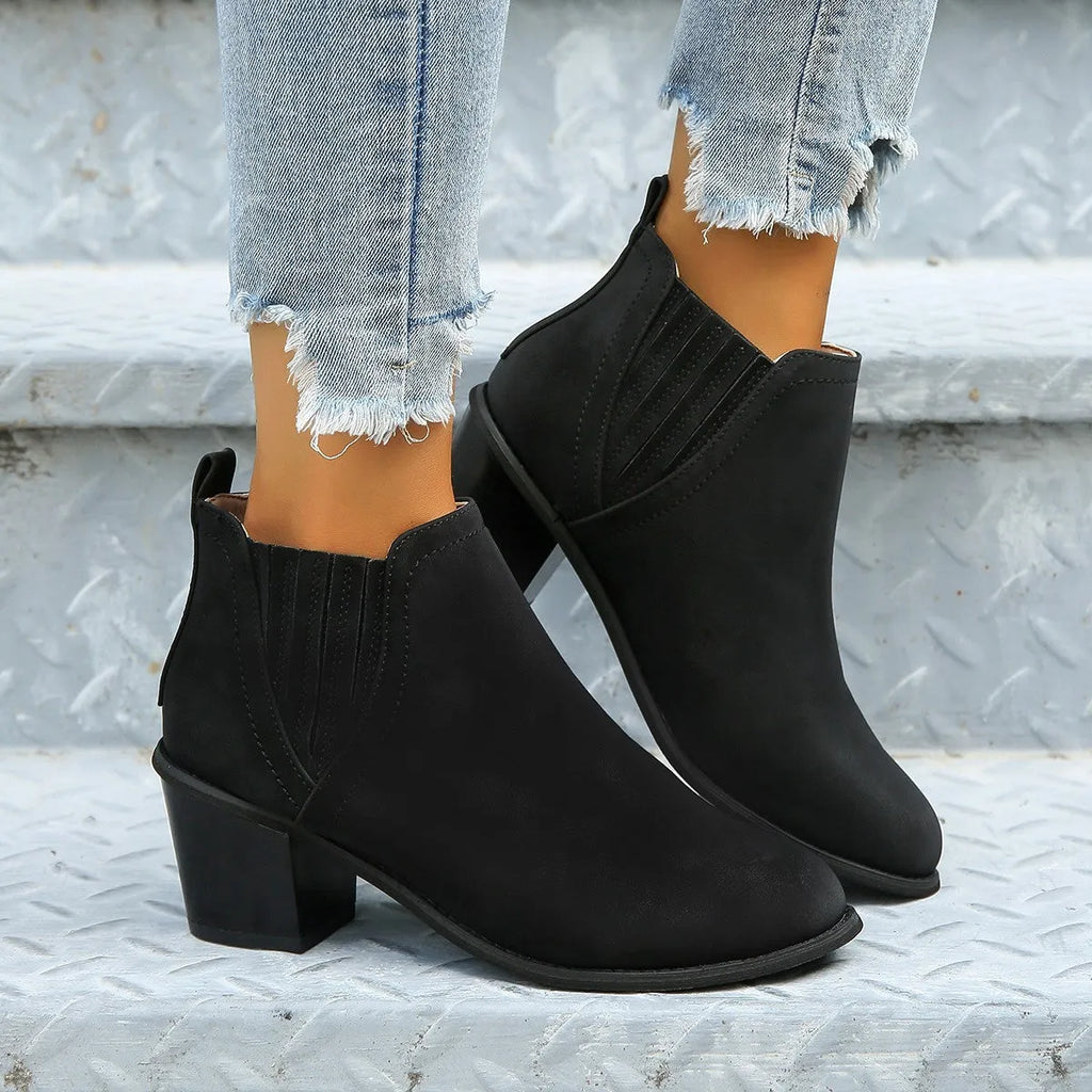 Women's black ankle boots with pointed toe and thick square heel on wooden floor