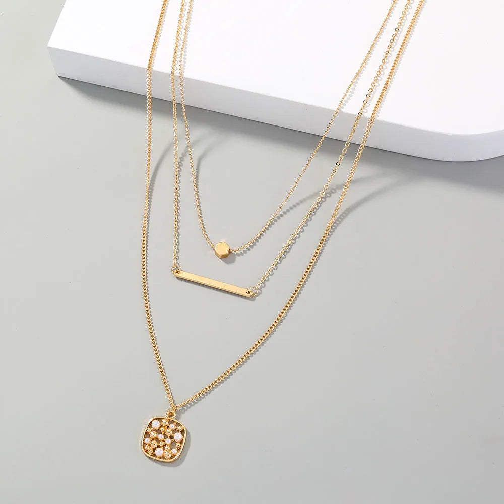 Gold multi-layer necklace with geometric pineapple pendant on a neutral background