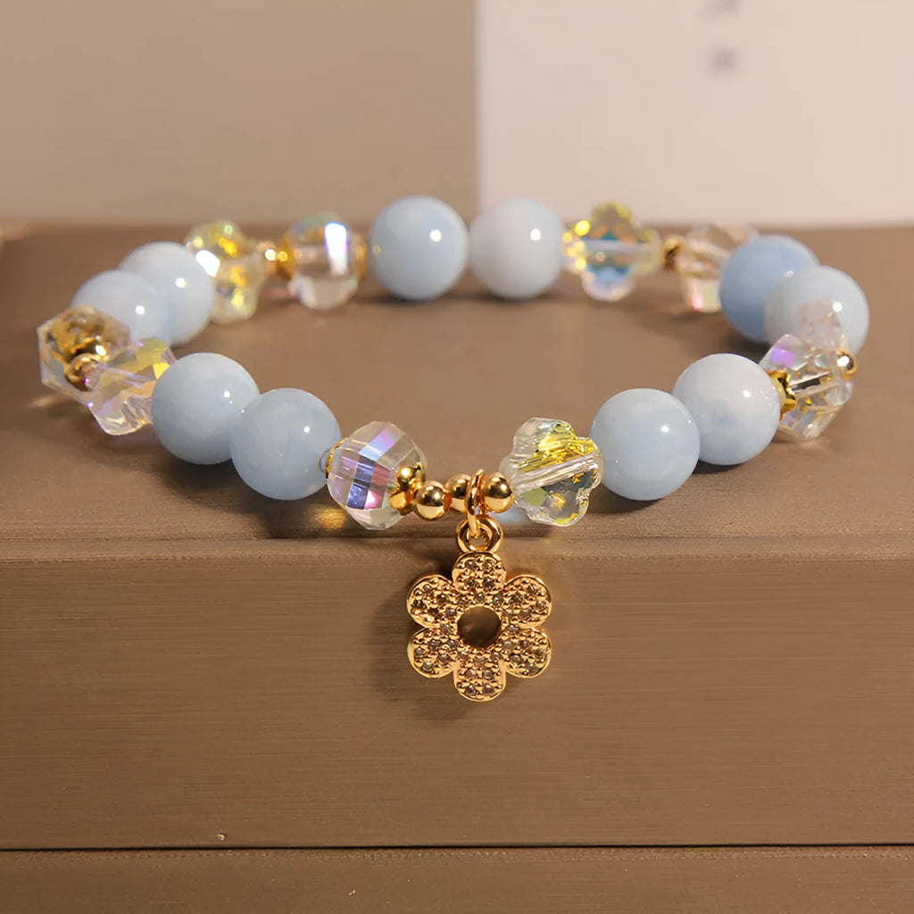 Women's bracelet with aquamarine crystal clover charm and white pearl details on a light background.