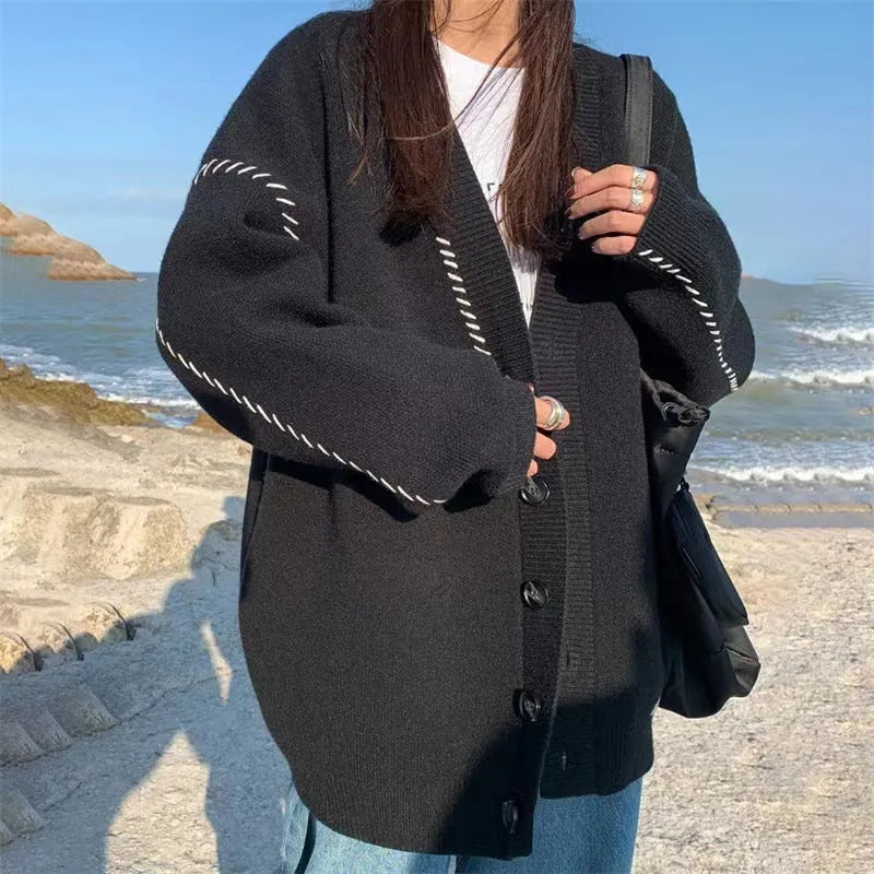 Women's loose fit black knitted cardigan coat with long sleeves on a hanger.