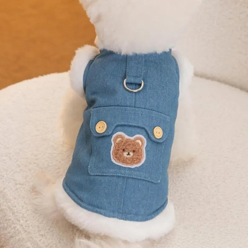 Denim dog vest with white wool lining, embroidered teddy bear patches, wooden buttons, and metal D-ring on blue background