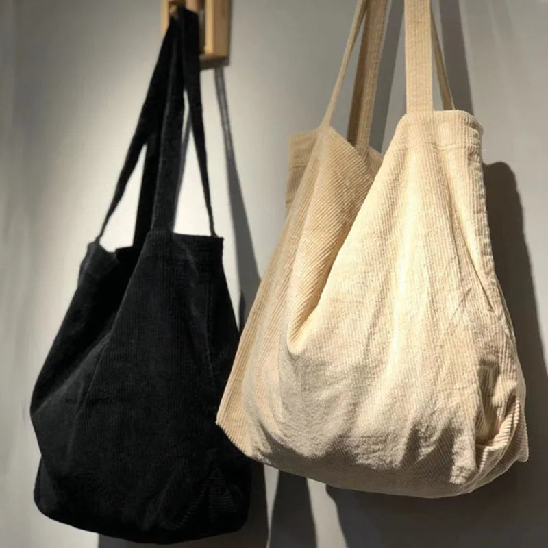 Large corduroy tote bag with soft handle, pleated detailing, and interior zipper pocket. Colour: black.