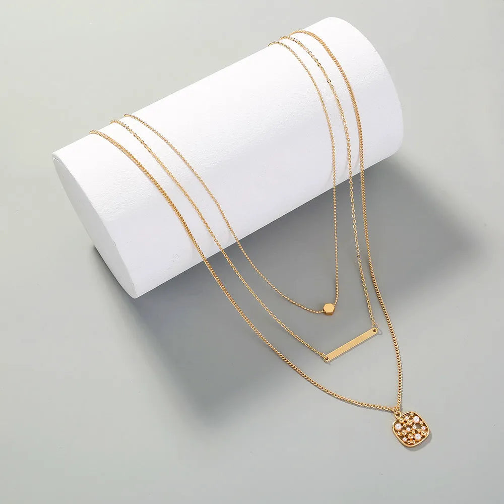 Gold multi-layer necklace with geometric pineapple pendant on a neutral background