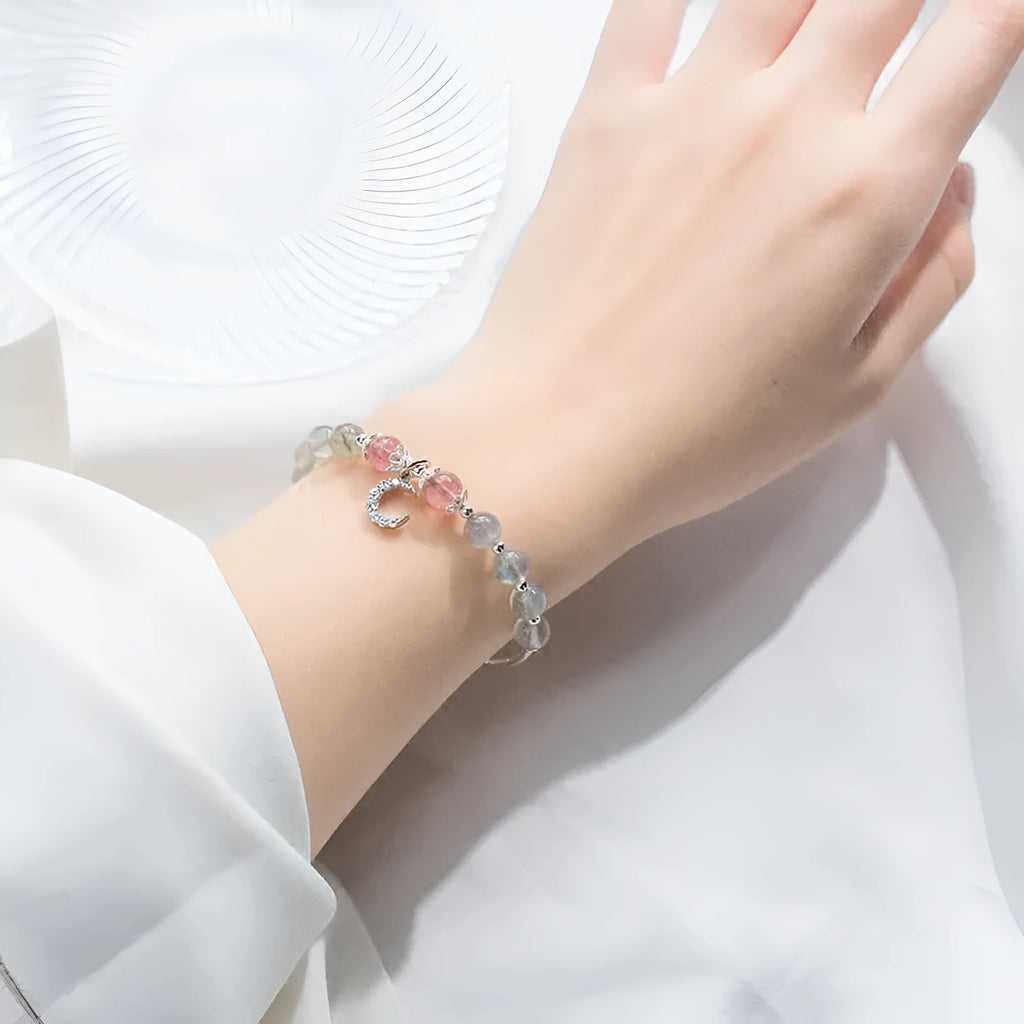 Handmade adjustable moonstone bracelet with crescent moon charm and crystal bead on a white background.