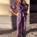 Women's floral print trousers suit with tie-neck puff sleeve top and matching trousers.