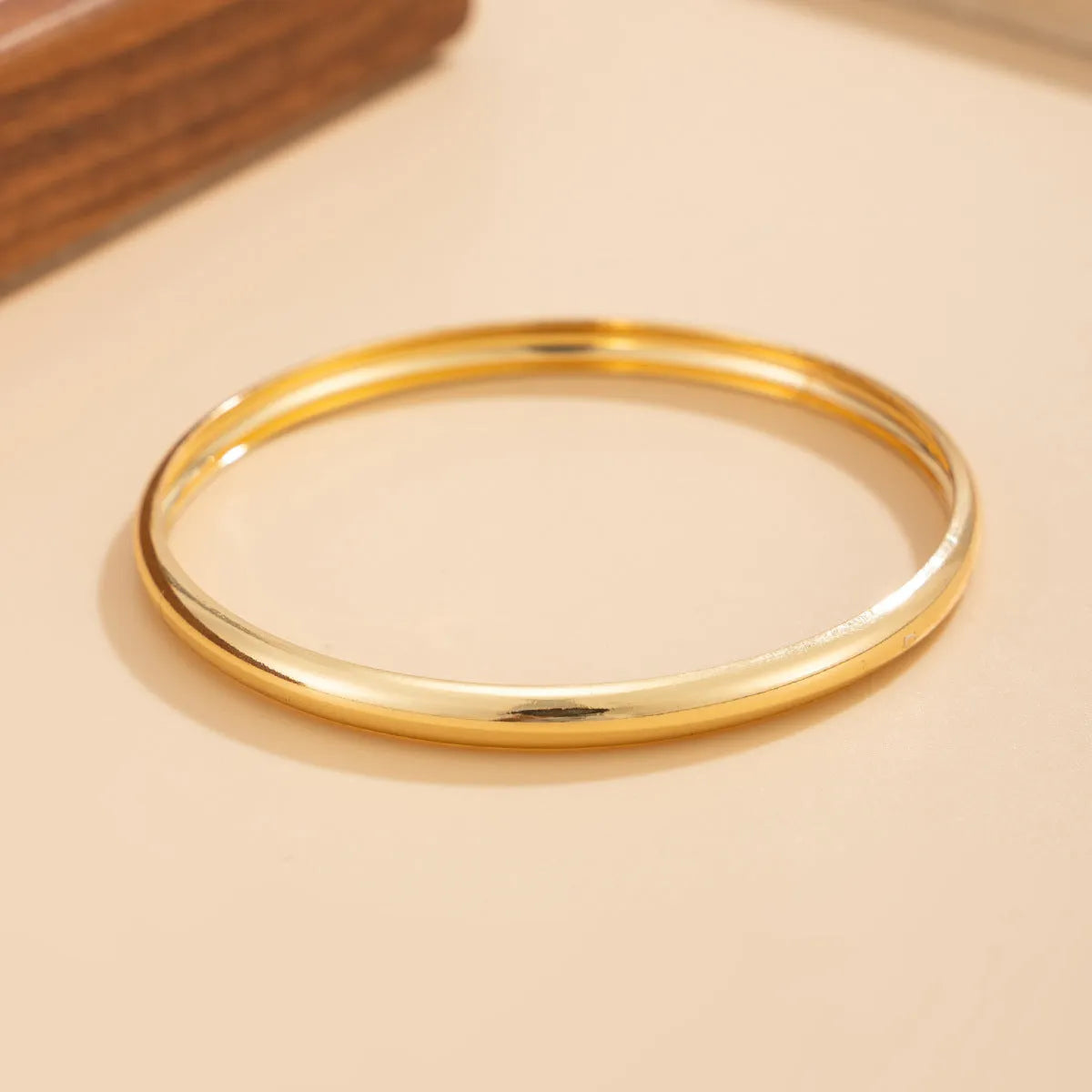 Exaggerated wide round glossy metal bracelet in gold tone on plain background