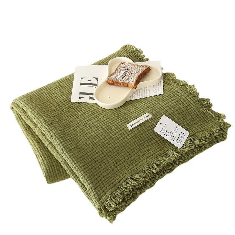 Cotton four-layer gauze blanket with tassel trim in various colours draped over a sofa.