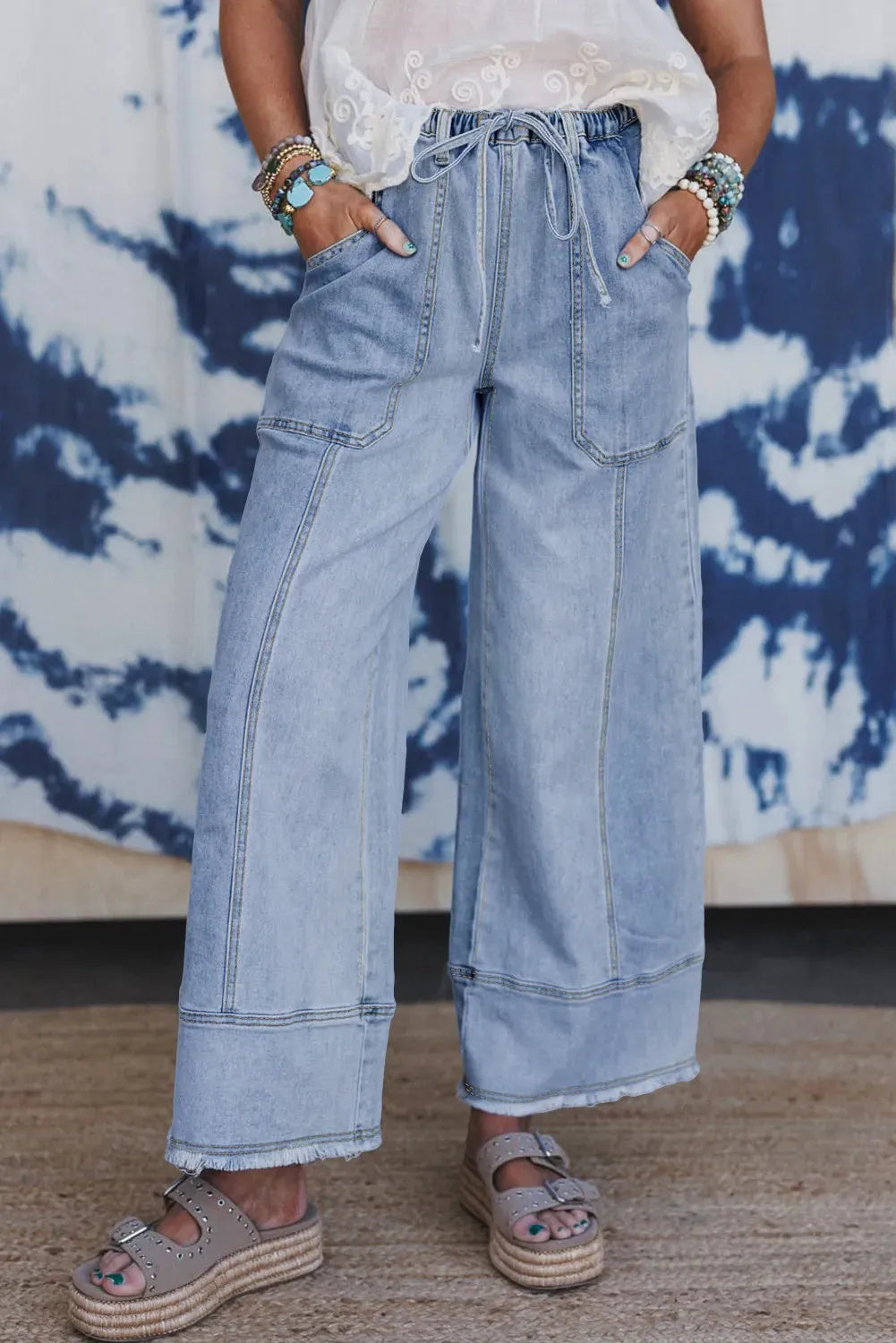 Beau blue wide leg denim trousers with drawstring waist and raw hem detail laid flat