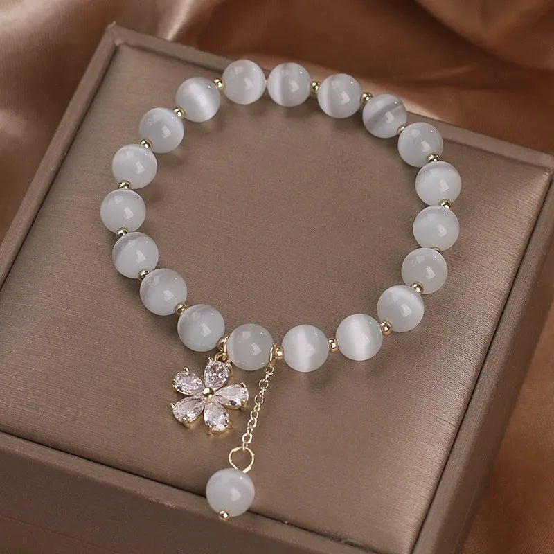Women's white cat's eye stone bracelet with flower and tassel charms on a single loop.