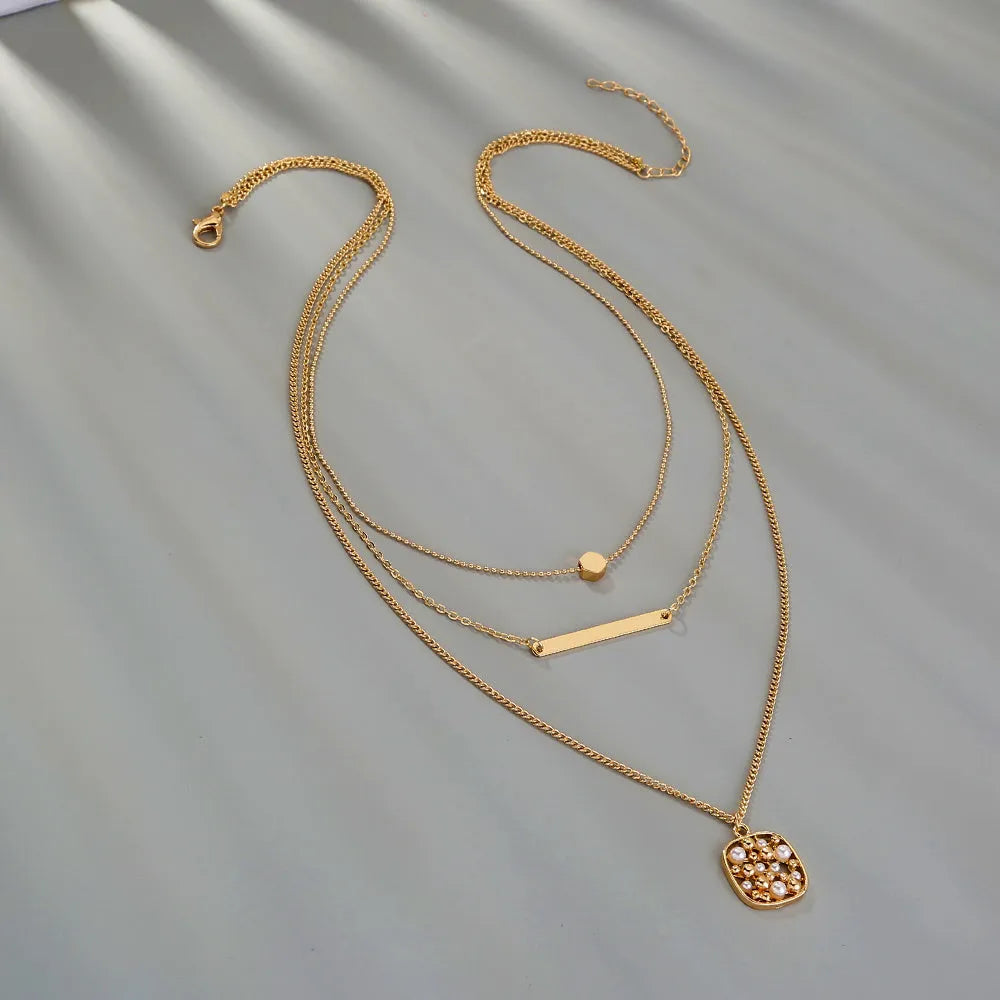 Gold multi-layer necklace with geometric pineapple pendant on a neutral background