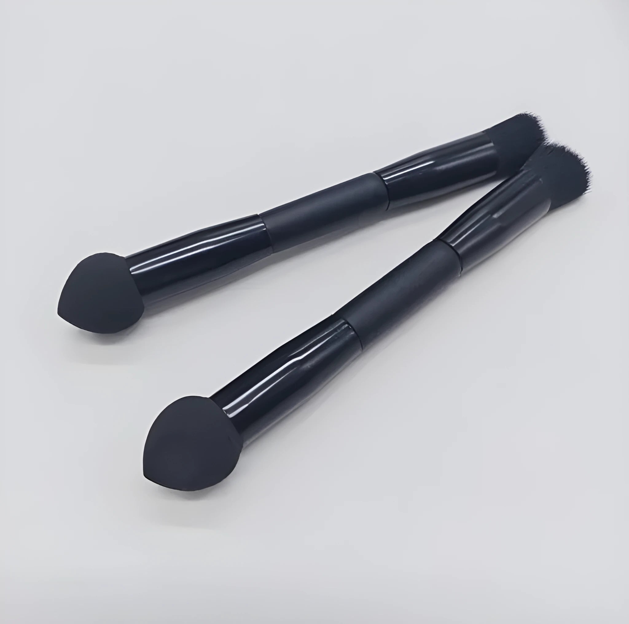 Double-headed black makeup brush with a pointed concealer brush on one end and an angled sponge on the other.