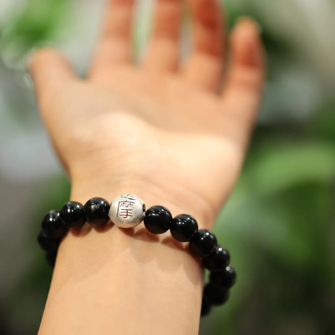 Close-up of a women's bracelet with large 10mm black agate beads and sterling silver details on a wrist.