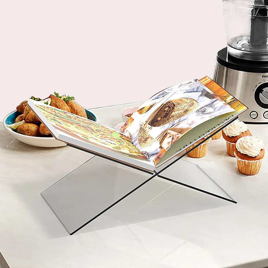 Clear acrylic X-shaped book display stand holding a hardback book on a wooden desk.