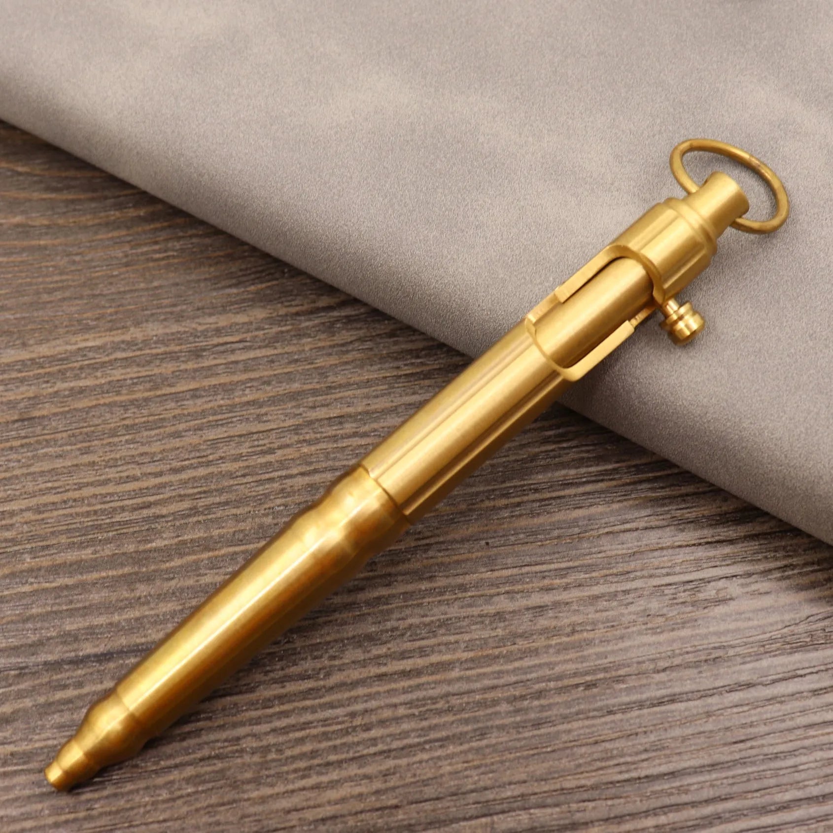 Close-up of a solid brass bolt action tactical pen with a press mechanism on a dark surface.
