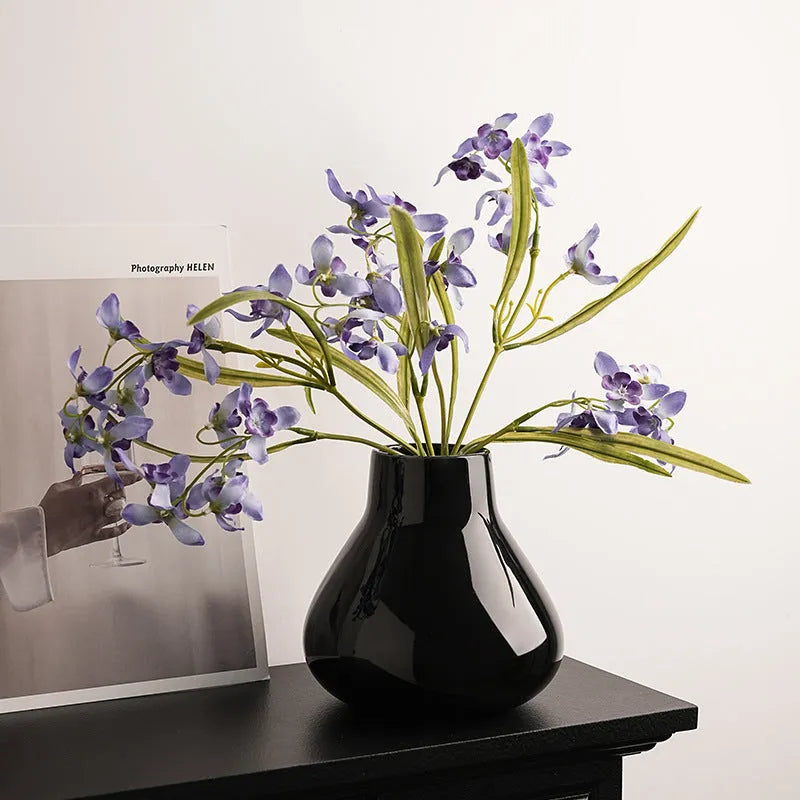 Black ceramic round belly vase with white artificial orchids on wooden table