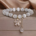 Women's white cat's eye stone bracelet with flower and tassel charms on a single loop.