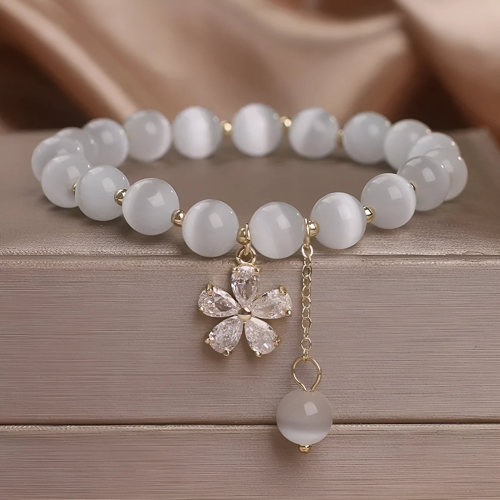 Women's white cat's eye stone bracelet with flower and tassel charms on a single loop.