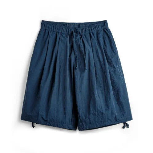 Prussian blue men's loose-fit nylon shorts with embroidery on a summer beach background.