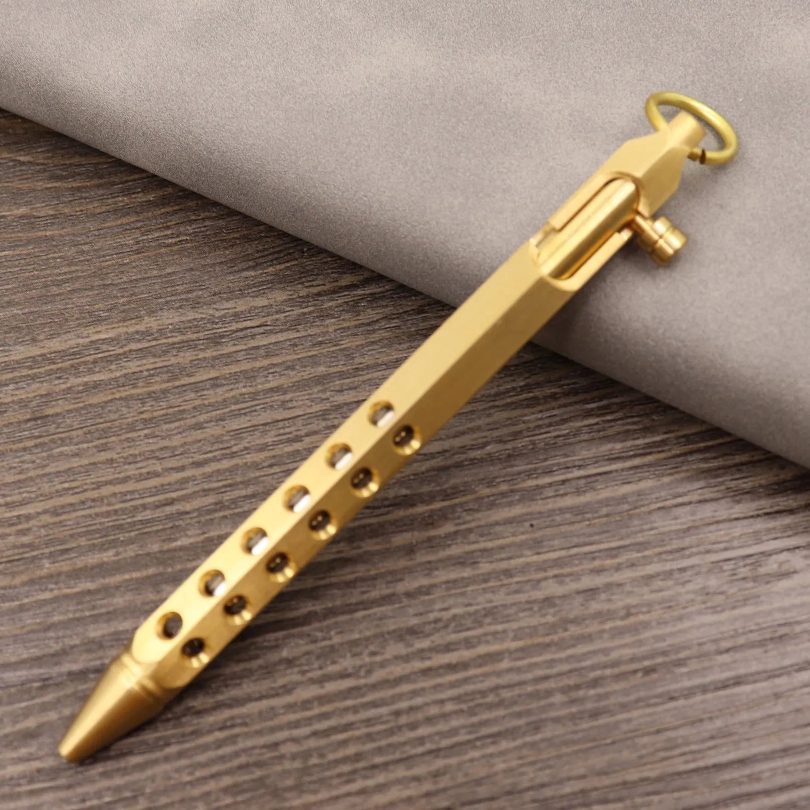 Close-up of a solid brass bolt action tactical pen with a press mechanism on a dark surface.