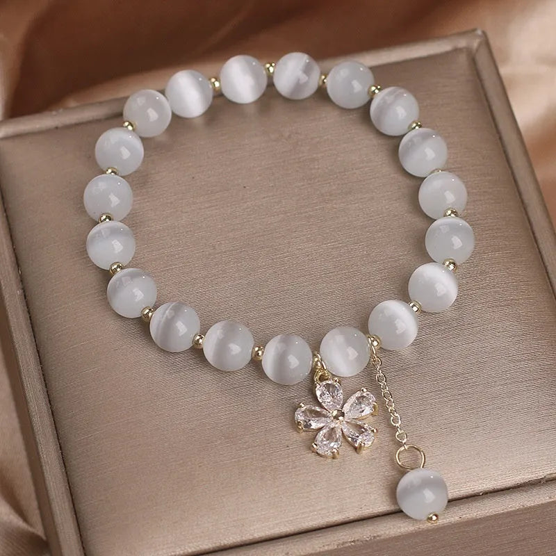 Women's white cat's eye stone bracelet with flower and tassel charms on a single loop.