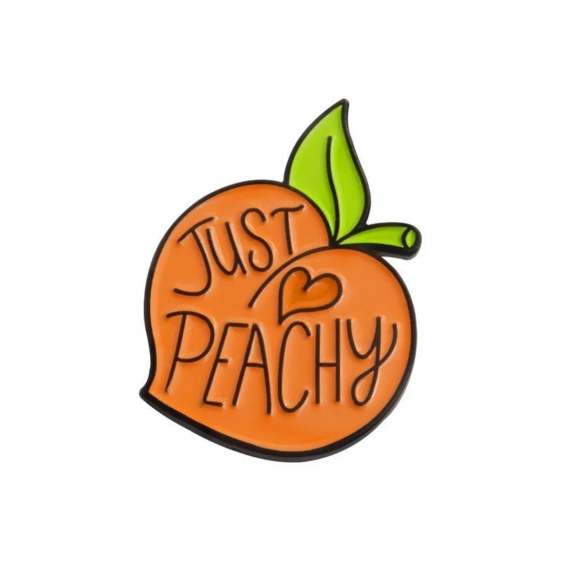 Colourful cartoon fruit and letter design metal brooch on a fabric background.