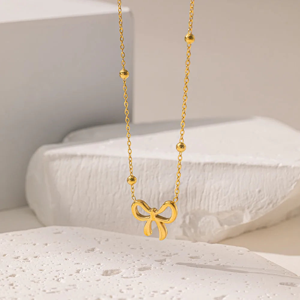 Gold bow necklace with titanium steel cross chain on white background