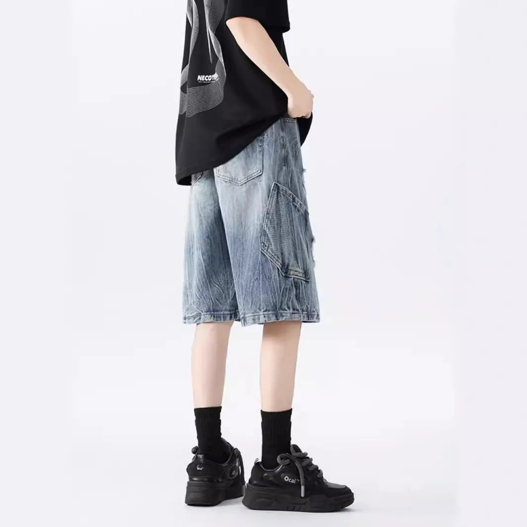 Man wearing loose blue ripped denim shorts with a vintage wash and distressed details.