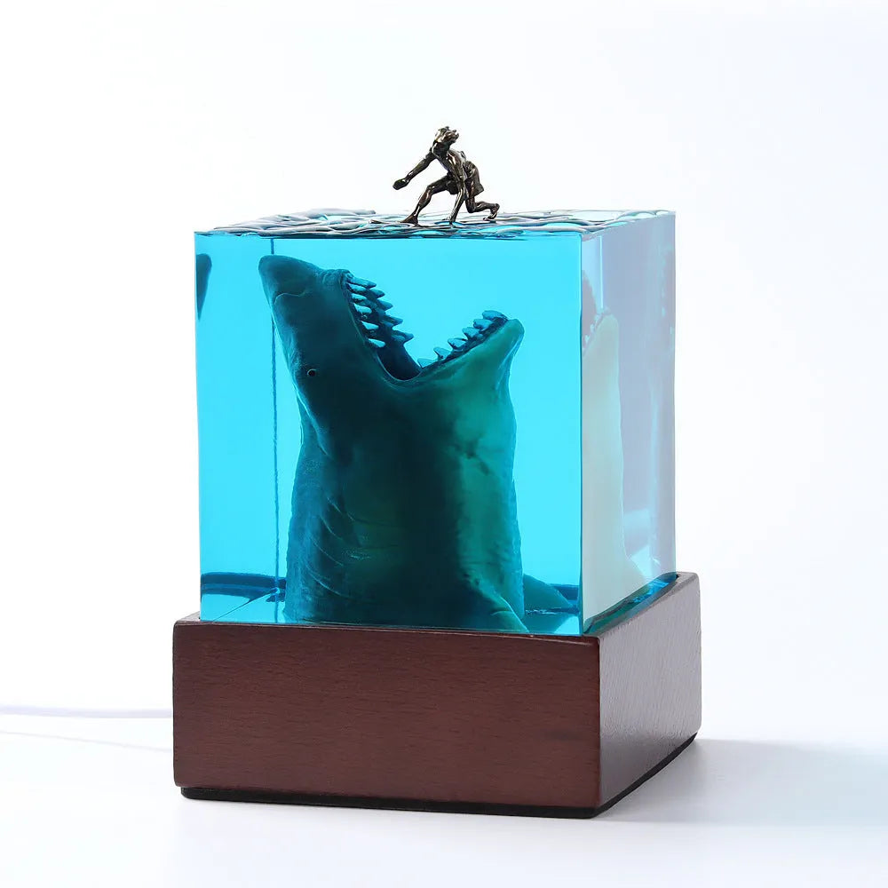 Close-up of a crystal resin shark surfer night light ornament on a dark surface.