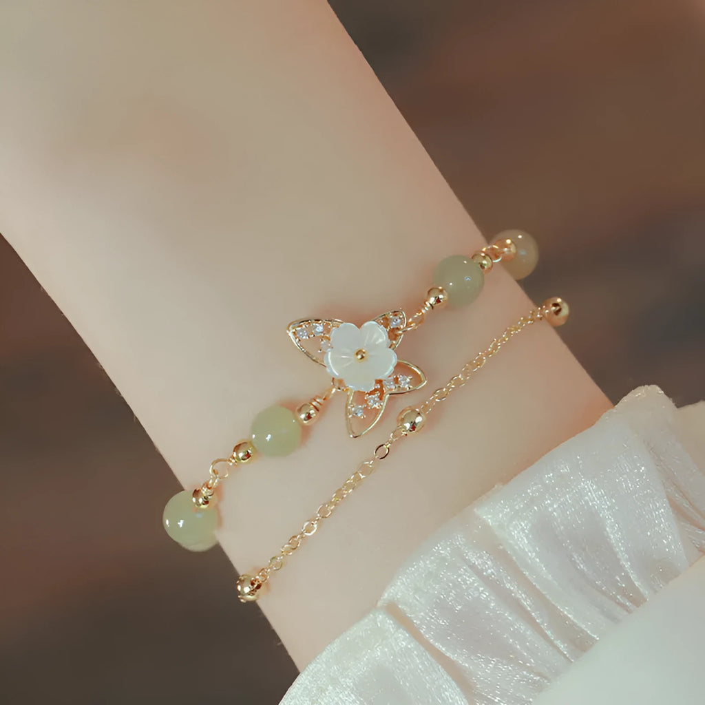 Yellow gold electroplated copper bracelet with a bells of Ireland butterfly, shell flowers, and Hetian jade accents.
