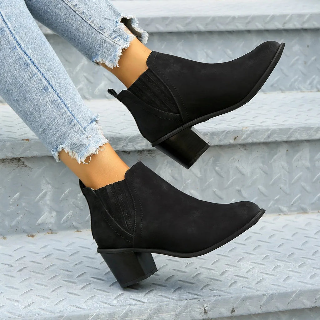 Women's black ankle boots with pointed toe and thick square heel on wooden floor