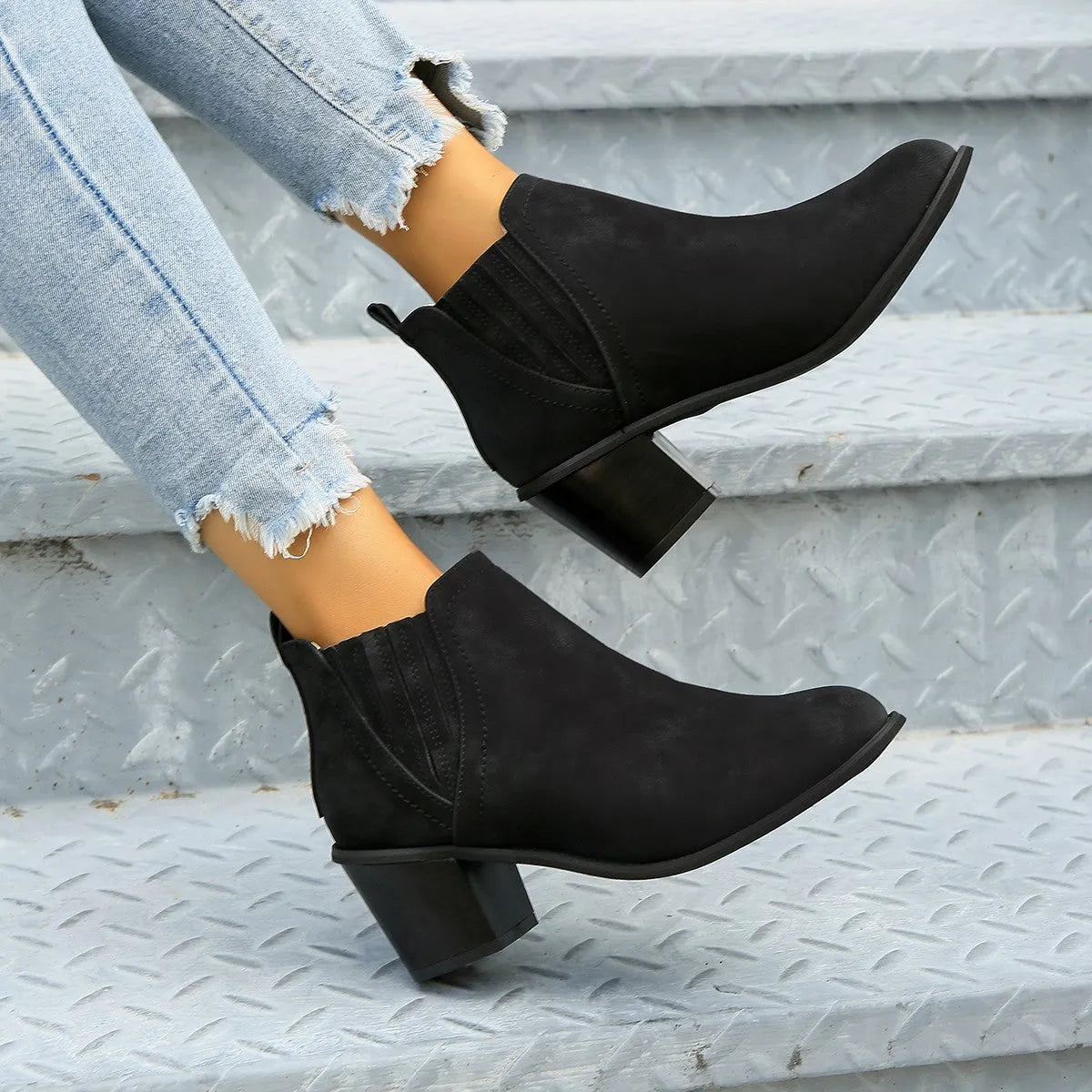 Women's black ankle boots with pointed toe and thick square heel on wooden floor