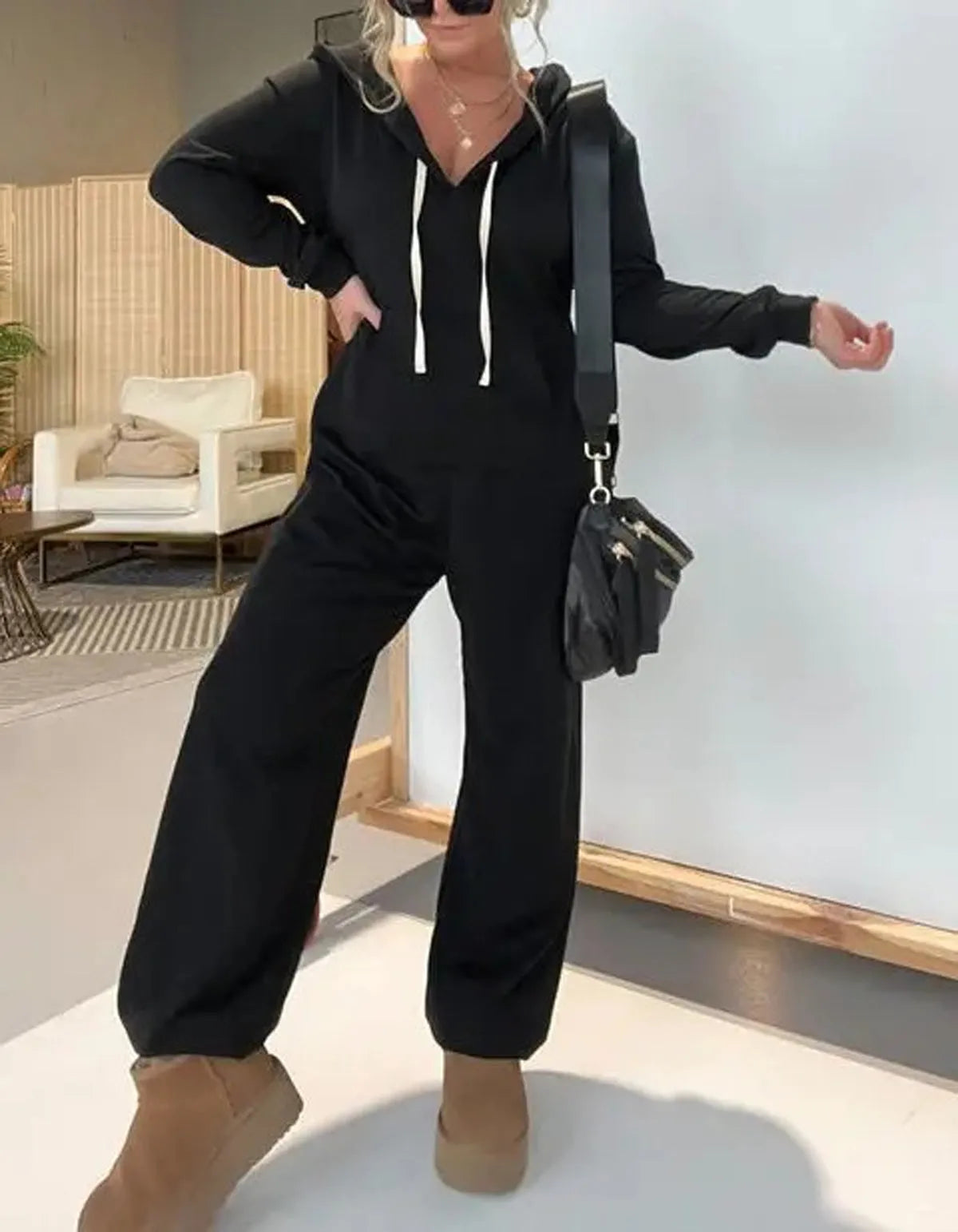Women's solid colour hooded jumpsuit in black with long sleeves and front pockets on a plain background