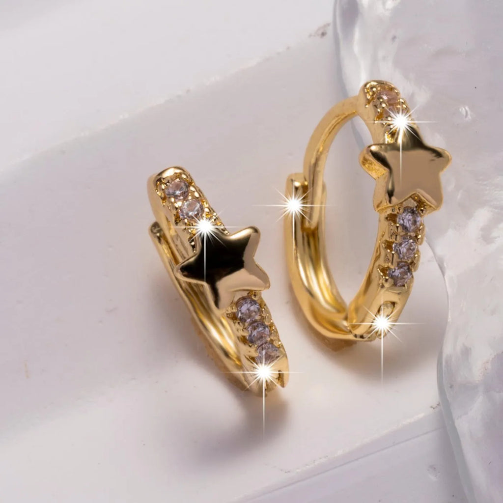 Gold copper five-pointed star earrings with inlaid zircon stones on a neutral background