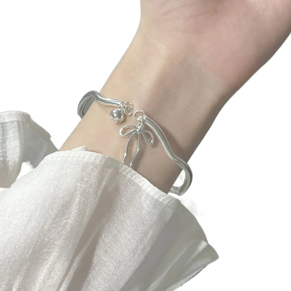 Silver tone adjustable bracelet with a bow charm on a white background.
