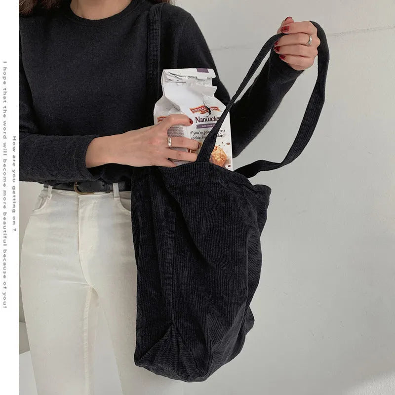 Large corduroy tote bag with soft handle, pleated detailing, and interior zipper pocket. Colour: black.