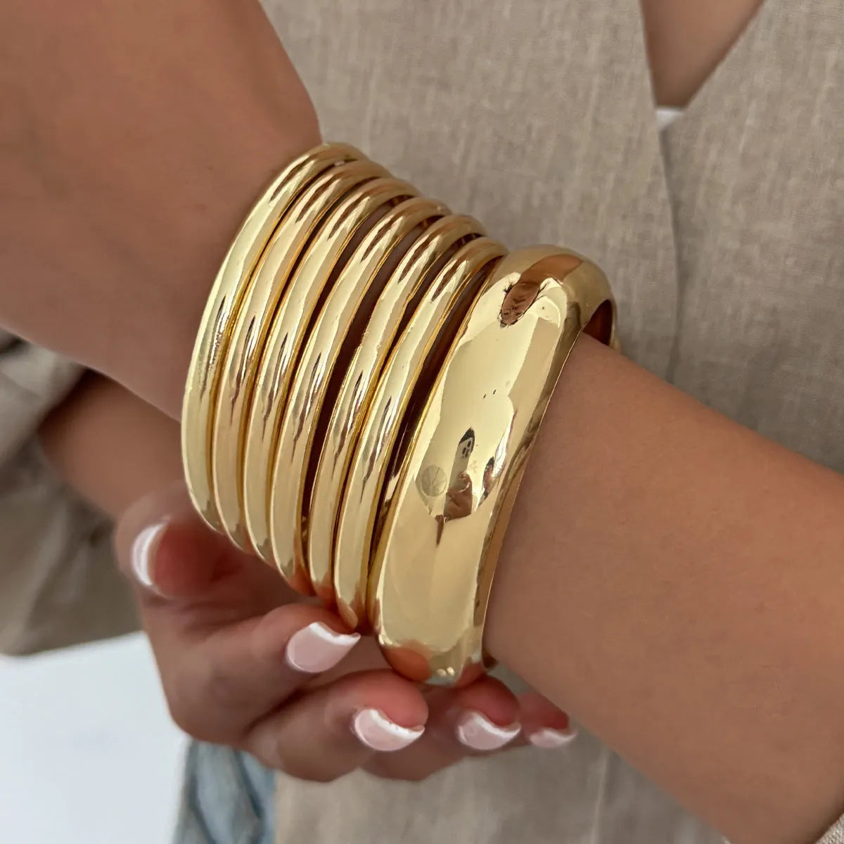 Exaggerated wide round glossy metal bracelet in gold tone on plain background