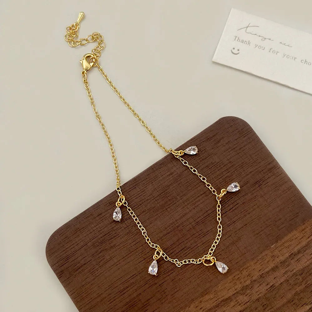 Women's zircon jewellery set showing geometric pendant necklace, matching earrings, and anklet on a white background.