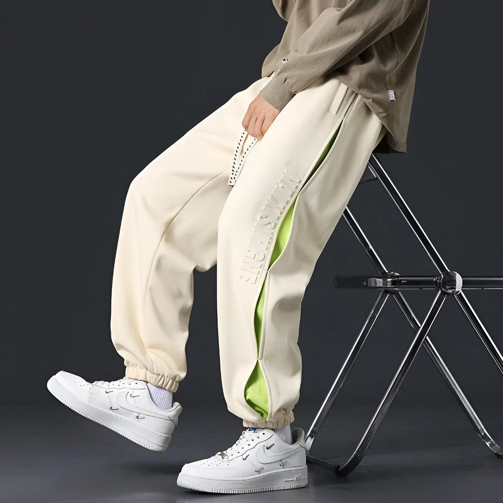 Men's loose black cotton trousers with white collage stitching print and banded ankle cuffs laid flat.