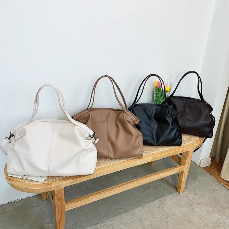 Large soft surface black messenger bag with soft handle and long shoulder strap on a table